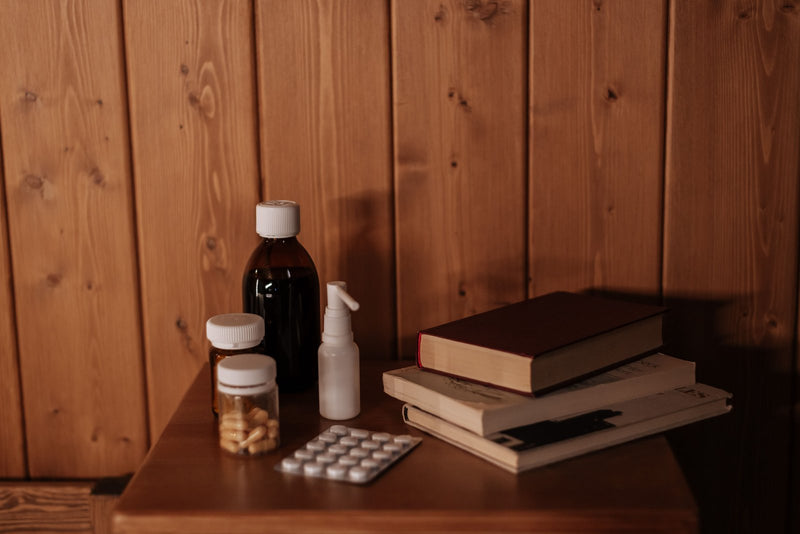 Pill bottles and a blister pack beside a stack of books on a bedside table
