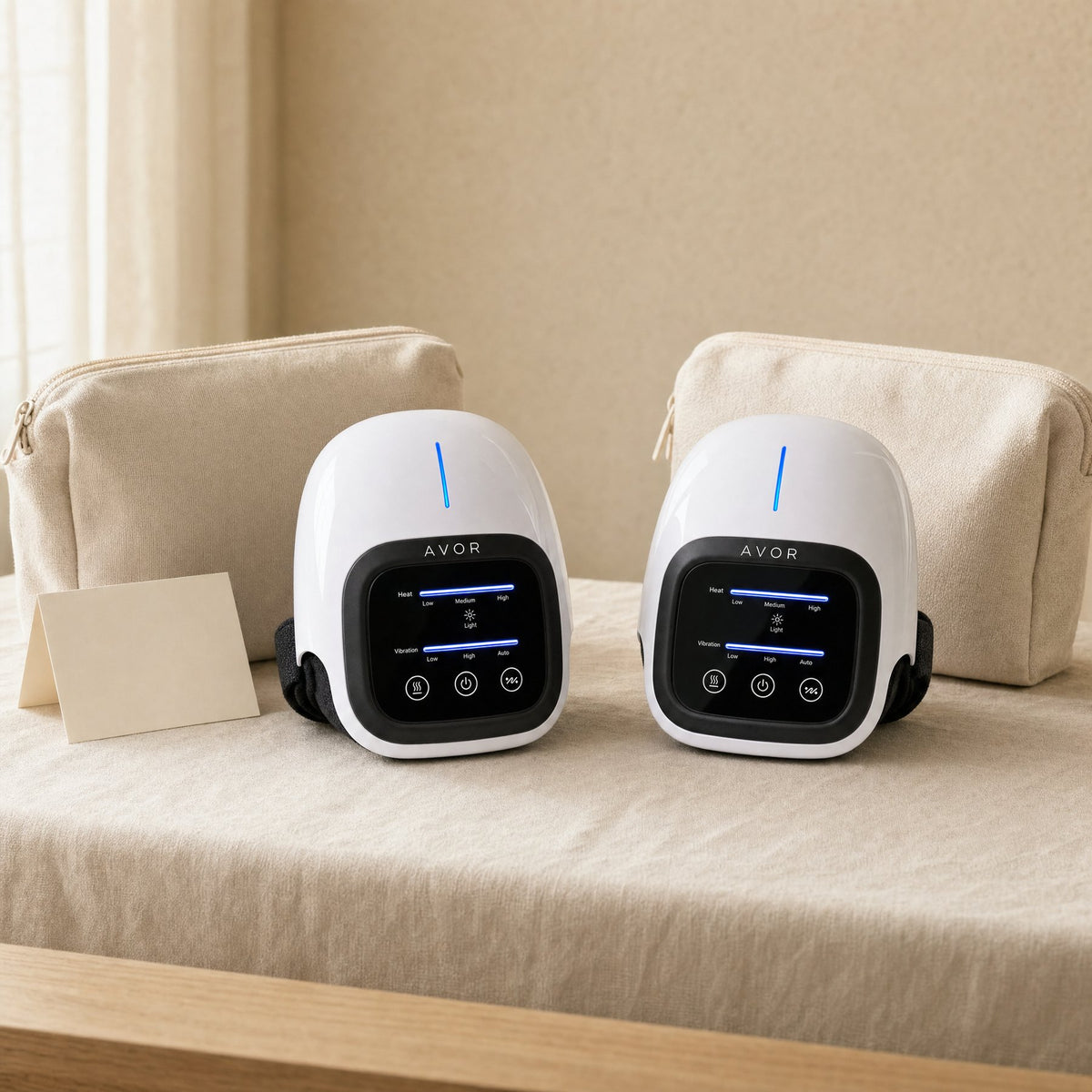 Two Avor heated knee massagers with travel pouches on a linen table