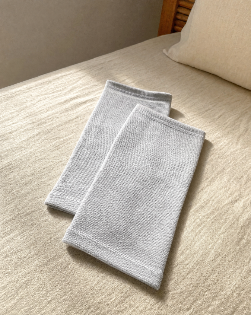 The pair of light grey knit knee sleeves folded on a bed in morning light