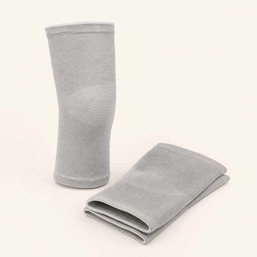 The pair of light grey knit knee sleeves, one standing upright and one folded flat, on a warm off-white background