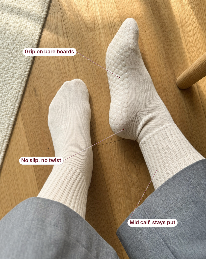 Two feet in ivory grip socks on a wooden floor, with labels reading grip on bare boards, no slip no twist, mid calf stays put